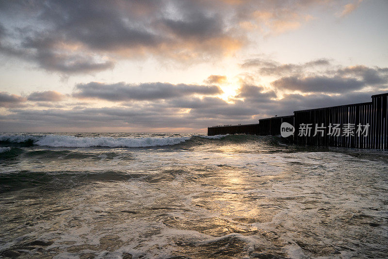 海滩和海浪的近景日落附近的国际边界墙在Playas Tijuana，墨西哥